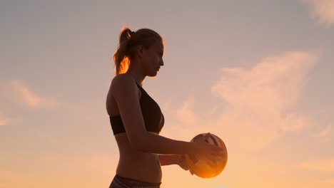 Eine-Schöne-Frau-Im-Bikini-Mit-Einem-Ball-Macht-Sich-Bei-Sonnenuntergang-Bereit,-Bei-Einem-Volleyballspiel-Im-Sand-Am-Strand-Einen-Aufschlagsprung-Zu-Machen.-Der-Entscheidende-Moment,-Der-Spannende-Moment-Des-Spiels-In-Zeitlupe.